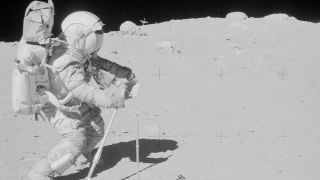 an astronaut in a bulky white suit walks on the dusty grey surface of the moon