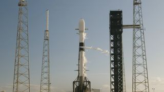 a white rocket sits upright on a launch pad venting vapor in the sunlight